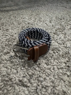 Blåvitt Flätat Bälte - Stilrent blåvitt bälte med spänne gjort av läder och metall. Skärpet är gjord av elastiskt material som anpassat efter behov. Längden är 105cm