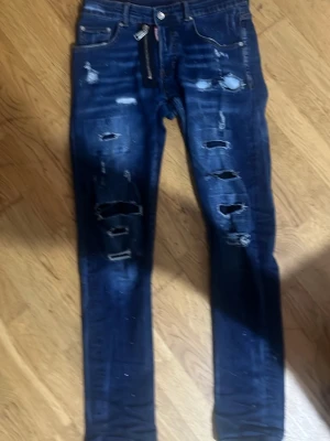 Mörkblå slitna skinny jeans från  - Säljer ett par mörkblå skinny jeans med flera slitningar och hål framtill för en riktigt edgy look. Klassisk femficksmodell med dragkedja och knapp. Jeansen har en tight passform och är gjorda i stretchigt denimtyg.