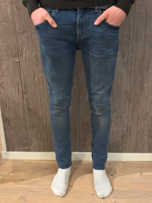Tiger of Sweden – Slim Fit Jeans Blue Denim (W30 L32) - Stilrena slim fit-jeans från Tiger of Sweden. Klassisk blå denim med snygg passform som funkar både till vardags och mer uppklätt. Sköna och i mycket bra skick.  ✔️ Storlek: W30 L32 ✔️ Modell: Slim Fit ✔️ Färg: Blå denim ✔️ Skick: Mycket bra skick, inga hål eller fläckar