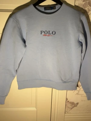 Ljusblå sweatshirt från Polo Ralph Lauren - Säljer en ljusblå sweatshirt från Polo Ralph Lauren med broderad logga på bröstet. Tröjan har rund halsringning, långa ärmar och är gjord i mjuk bomull. Perfekt för en chill och stilren look.