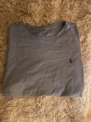 Blå t-shirt från Polo Ralph Lauren - Säljer en stilren blå t-shirt från Polo Ralph Lauren med klassisk rund hals och diskret broderad logga på bröstet. T-shirten är i mjuk bomull och har korta ärmar, perfekt till jeans eller shorts. (Förlåt för bilderna, lite knöliga)