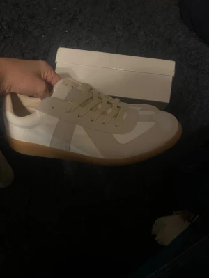 Snygga sneakers beige/vit - Snygga sneakers i beige och vitt med klassisk gummisula. Ovandel i lammnappa och mocka, med snygga ton-i-ton paneler och snörning. Perfekta för dig som gillar minimalistisk och clean stil. Storlek 43 använda 1 gång