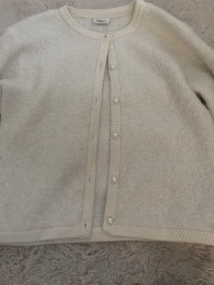 Beige kofta från Kappahl med pärlknappar - Supermysig beige kofta från Kappahl i storlek 158/164. Koftan har pärlknappar framtill och dekorativa kanter i fiskbensmönster. Perfekt för lager på lager och passar till många outfits. Materialet känns mjukt och fluffigt.