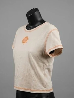Beige croppad t-shirt med soltryck - Beige croppad t-shirt med orangea kontrastsömmar och ett soltryck i orange framtill. Rund halsringning och korta ärmar. Tillverkad i mjuk bomull som känns skön mot huden. Perfekt för en chill och avslappnad stil.