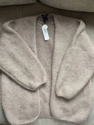 Beige stickad kofta från Lindex - Mysig beige stickad kofta från Lindex med öppen front och avslappnad passform. Koftan har lång ärm och är tillverkad i ett mjukt, fluffigt material som passar perfekt för lager-på-lager. Enkel och stilren design som är lätt att matcha. Slutsåld överallt!!!! Inte använd, prislapp kvar! 