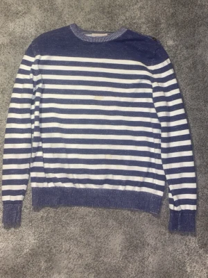 Stickad Tröja - Säljer en klassisk långärmad tröja från Murrey i blått och vitt med horisontella ränder. Tröjan har rund halsringning och ribbade muddar vid ärmslut och nederkant. Perfekt för dig som gillar en avslappnad och tidlös stil. Modellen är 184cm lång