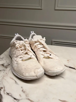 Vita Nike Free sneakers med flätad design - Säljer ett par vita Nike Free sneakers med unik flätad ovandel och klassisk snörning. Skorna har en lätt och flexibel sula, rund tå och diskreta detaljer. Perfekta för dig som gillar stilrena och sportiga sneakers med twist.