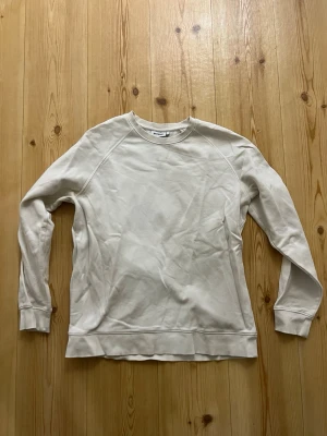 Cremefärgad sweatshirt från Weekday - strl.L - En stilren vit sweatshirt från Weekday i storlek L. Tröjan har rund halsringning, långa ärmar och ribbade muddar vid ärmslut och nederkant. Tillverkad i mjuk bomull för en skön och avslappnad look.