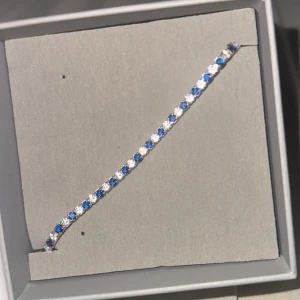 Silver armband med blå och vita stenar - Snyggt och stilrent tennisarmband i silverfärgad metall med glittrande blå och vita stenar i rad. Perfekt för dig som gillar att sticka ut med lite färg och bling. Armbandet har en klassisk och tunn design som passar till många olika looks. Dessutom glänser och ser mycket bättre ut i verkligheten! 