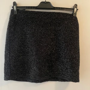 Svart glittrig minikjol - En svart glittrig minikjol från Vila. Den har en underkjol som gör att den inte är genomskinlig samt resår i midjan. Storlek S men på mig som normalt är en M sitter den jättebra! 