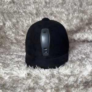 Svart ridhjälm Euro-Lite - Säljer en klassisk svart ridhjälm från Euro-Lite med matt yta och ventilerande detaljer framtill. Hjälmen har justerbart hakband och mjuk insida för extra komfort. Perfekt för dig som vill ha en stilren och säker look i stallet.