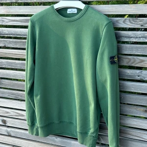 Grön sweatshirt från Stone Island - Säljer en grön sweatshirt från Stone Island med klassisk rund hals och ribbade muddar. Tröjan har den ikoniska loggan på vänster ärm och är tillverkad i mjuk bomull. Sicket är 8,5/10 