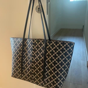 Malene Birger  - Stor och rymlig väska från Malene Birger. Väskan har långa, smala axelband i svart och är perfekt för att bära med sig allt man behöver under dagen. Väskan har slitning på axelremmen men är annars jättefin. 