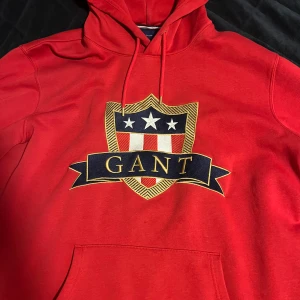 Röd hoodie från GANT - Riktigt snygg röd hoodie från GANT med flera snygga detaljer. Storlek 3XL men sitter som XL-XXL. Jättebra kvalite, inga defekter. Inprincip nyskick!  Bara att skriva vid funderingar, Skicka ett prisförslag om priset inte skulle duga:)