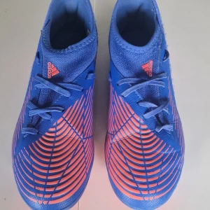 Adidas Predator blå fotbollsskor storlek 37 2/3 - Snygga Adidas Predator fotbollsskor i blått med orange detaljer och mönster. Skorna har snörning, låg profil och mönstrad ovandel för extra grepp på planen. Perfekta för dig som vill sticka ut på matchen! Ord pris. 250