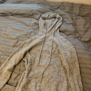 Kashmir Grå stickad hoodie med huva - Mysig grå stickad hoodie med långa ärmar och huva med snörning. Perfekt för kyliga dagar och enkel att matcha med jeans eller mjukisbyxor. Tröjan har en avslappnad passform och är tillverkad i ett mjukt material som känns skönt mot huden.