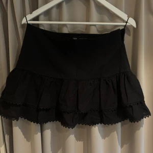 Svart volangkjol från Zara - Supersöt svart kjol från Zara med dubbla volanger och spetskant längst ner. Den är oanvänd. Kjolen har en dragkedja i sidan. 
