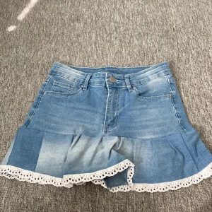 Blå jeanskjol med volang och spets - Supersöt ljusblå jeanskjol med volangkant och vit broderad spets längst ner. Sytt den själv av ett par jeans. Inte kommit till användning