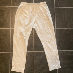 Vita mjukisbyxor med snörning - Snygga vita mjukisbyxor med elastisk midja och snörning. Byxorna har fickor på sidorna och med diskret guld loga. Finns med matchande överdel (dress)