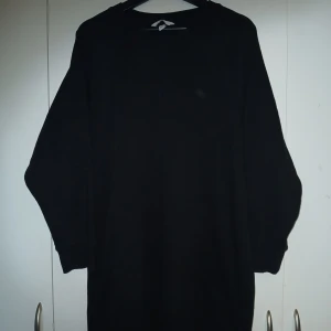 Svart långärmad klänning - En svart, enkel och stilren bomullsklänning med lång ärm. Perfekt för dig som gillar en clean look och vill ha något som funkar till många outfits. Klänningen har en loose fit passform och är mjuk och skön att bära.