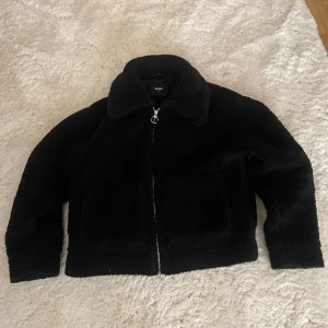 Svart teddyjacka från Bik Bok XS - Mysig svart teddyjacka från Bik Bok i storlek XS. Jackan har en klassisk krage, två stora fickor framtill och stängs med en silvrig dragkedja med ringdetalj. 