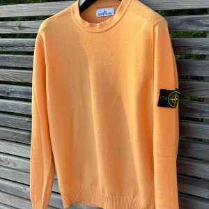 Orange stickad tröja från Stone Island - Säljer en orange stickad tröja från Stone Island med klassisk patch på ärmen. Tröjan har rund halsringning, sicket är helt perfekt och en 10/10 