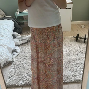 Populär långkjol - Säljer en långkjol från Marta de chateu med färgglatt paisleymönster i rosa, lila, beige och grönt. Kjolen har smock i midjan och är gjord i ett lätt och luftigt material, perfekt för varma dagar. Superfin att styla med en enkel topp eller stickad tröja. Säljer eftersom den ej kommer till andvändning!☀️