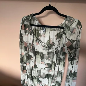 Supernajs blus 💘 - Snygg långärmad blus  med abstrakt mönster i grönt, rosa och vitt. Blusen har snörning vid halsringningen och en avslappnad passform. Perfekt för dig som gillar unika prints och bekväma plagg. ❤️❤️