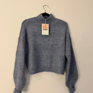 Blå stickad tröja från ONLY - Blå stickad tröja från ONLY med hög hals och långärmad modell. Tröjan är lite kortare i längden.