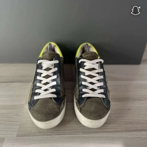 Feta sneakers från Philipe model - Snygga sneakers med camouflage-mönster i gröna och bruna toner, svarta skinnpaneler och detaljer i mocka. Skorna har vita snören och en cool neon-gul häl. Perfekt för dig som vill sticka ut med streetstyle-vibe.