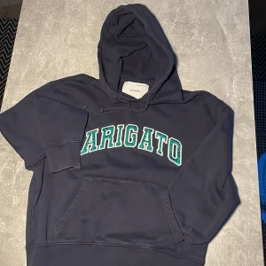 Mörkblå hoodie från Axel Arigato - Snygg mörkblå hoodie från Axel Arigato med stor grön och vit logga framtill. Klassisk känguruficka, huva med snörning och ribbade muddar. Perfekt för en chill och trendig look.