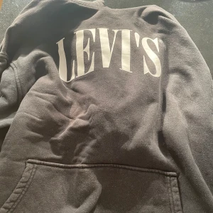 Svart hoodie från Levi's i storlek M - Svart hoodie från Levi's med stor vit logga på bröstet. Tröjan har känguruficka framtill och en relaxed passform. Perfekt för dig som gillar en enkel och klassisk streetstyle-look.