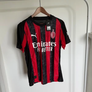 AC Milan Puma matchtröja 25/26  - AC Milan matchtröja från Puma i röd och svart med klassiska vertikala ränder. Tröjan har klubbmärke på bröstet, Puma-loggor och sponsortryck. Tillverkad i lätt och ventilerande polyester, perfekt för fotboll eller supporterliv.