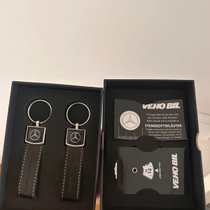 Mercedes-Benz nyckelringar i svart läder - Två snygga nyckelringar från Mercedes-Benz i svart läder med vita sömmar och silverfärgad metall. Klassisk Mercedes-logga framtill och stilren design. Perfekt accessoar för bilnycklar eller som present till bilälskaren.