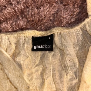 Gul volang-linnetopp från Gina Tricot - Supersöt ljusgul linnetopp från Gina Tricot med tunna axelband och flera lager volanger. Toppen har v-ringning och är gjord i ett lätt, transparent tyg som känns perfekt för varma dagar. Perfekt att styla med jeans eller kjol för en fräsch look.