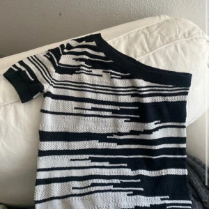 Randig offshoulder topp från Lindex - Snygg stickad topp från Lindex i svart och vitt med coolt randigt mönster. Modellen är offshoulder med kort ärm. 