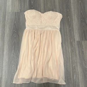 Ljus axelbandslös spetsklänning - Superfin ljus kortklänning med axelbandslös design och vadderad byst. Överdelen är täckt av spets och midjan markerad med ett satinband. Kjolen är lätt och luftig i flera lager. Perfekt för dig som vill ha en romantisk och söt look.