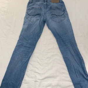Blå Tapered Mike jeans från Jack&Jones - Snygga blå jeans från Selected i modellen Tapered Mike. Jeansen har klassisk femficksdesign, dragkedjegylf och avsmalnande ben. Tillverkade i mjukt denimtyg med en ljus tvätt som ger en fräsch och avslappnad look.