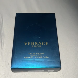 Versace Eros Eau de Toilette 100ml - Versace Eros Eau de Toilette 100ml med ikonisk turkosblå glasflaska och guldiga detaljer. Flaskan har en fyrkantig form med Medusa-huvudet ingraverat och levereras i en lyxig blå kartong med guldfärgade tryck. En klassisk och fräsch doft från Versace.