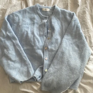 Ljusblå kofta från Gina Tricot - Supermysig ljusblå kofta från Gina Tricot i ullblandning. Koftan har rund halsringning, ribbade muddar och knäppning med flera knappar framtill. Perfekt för lager-på-lager och chill dagar. Långärmad och riktigt skön att ha på sig.