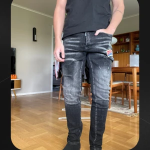 Dsquared2 1964-patch ”Cool Guy Jean” - Säljer ett par jeans från Dsquared2, färgad Dsq2 1964-patch på ena låret. Svart denim med blekta partier, slitna detaljer och revner i tyg. Slim eller skinny-fit, med knappstängning (flera knappar) och stretch i tyget. Är storlek medium/33, passar dig som är 175-185. Använda en gång, helt perfekt skick, aldrig tvättade.