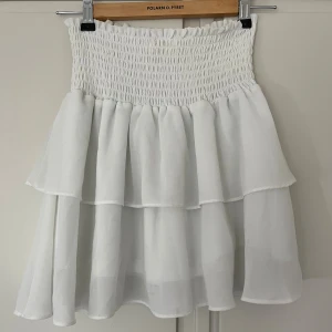 Vit volangkjol från Chelsea - Supersöt vit kjol från Chelsea med smockad midja och dubbla volanger. Storlek XXS men passar även XS och S