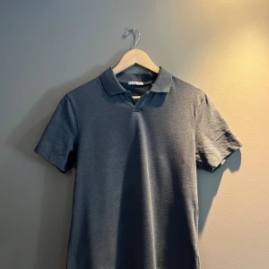 Mörkgrå pikétröja från Bläck - Snygg mörkgrå pikétröja från Bläck i klassisk modell med krage och kort ärm. Perfekt för dig som gillar en stilren och enkel look. I storlek S så lite liten för mig. Köpt på MQ.