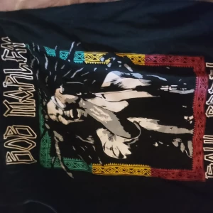 Bob Marley ärmlös t-shirt - Säljer en svart ärmlös t-shirt med stort Bob Marley-tryck på framsidan. Färgglada detaljer i rött, gult och grönt runt motivet. Perfekt för dig som gillar musik och vill sticka ut med en cool och bekväm look.