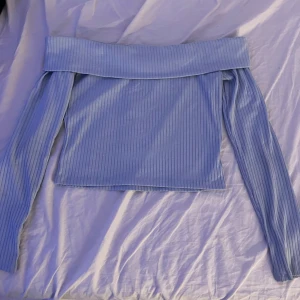 Ljusblå offshoulder ribbad topp - Säljer en ljusblå offshoulder topp med långa ärmar. Toppen är ribbad och har en bred kant upptill som ger en snygg och trendig look. Perfekt för dig som gillar stilrena och enkla plagg med en twist.