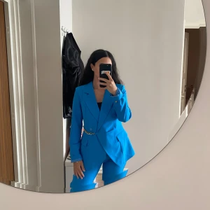 Blå kavaj och byxa från NOIX - Säljer ett set från NOIX med kavaj och matchande byxa i klarblå färg. Kavajen har snygg passform, breda slag, guldiga knappar och en kedjedetalj i midjan. Byxorna är raka och stilrena. Perfekt för dig som vill sticka ut med färg! Aldrig använda, prislapp finns kvar.