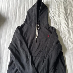 Svart hoodie från Polo Ralph Lauren XL - Svart hoodie från Polo Ralph Lauren i storlek XL. Klassisk design med huva, dragsnören och känguruficka. Liten röd broderad logga på bröstet. Perfekt för chill dagar och enkel att matcha med jeans eller joggers.