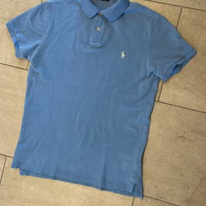 Blå pikétröja från Ralph Lauren S - Snygg blå pikétröja från Polo Ralph Lauren i modellen Custom Fit. Klassisk krage med två knappar och broderad logga på bröstet. Tillverkad i 100% bomull, perfekt för en chill och stilren look.