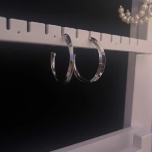 Stora silvriga hoops örhängen från Astrid och Agnes  - Säljer ett par stora, klassiska hoops örhängen i blankt silverfärgat material. De har en rund och stilren form som ger en cool vibe till din look. Perfekta för dig som gillar enkla men snygga accessoarer.