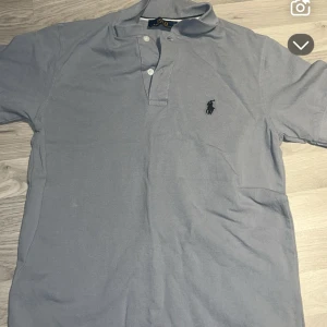 Ljusgrå Polo Ralph Lauren t-shirt S - Snygg ljusgrå t-shirt från Polo Ralph Lauren i storlek S. Klassisk pikémodell med korta ärmar, krage och två knappar framtill. Ikoniska broderade loggan på bröstet. Tillverkad i mjuk bomull som är skön mot huden.